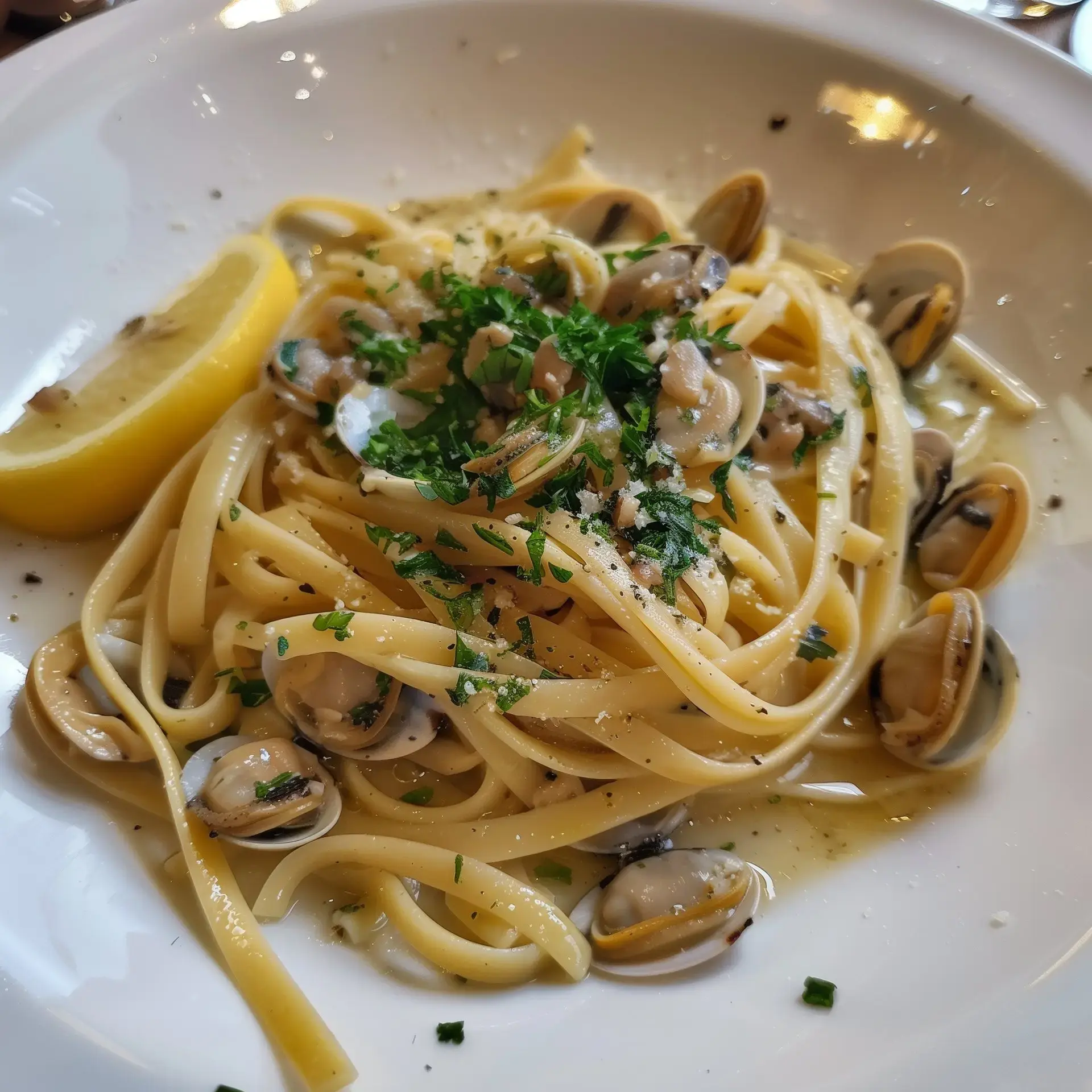 Un plat de linguine aux palourdes garni de persil et accompagné d'une tranche de citron.