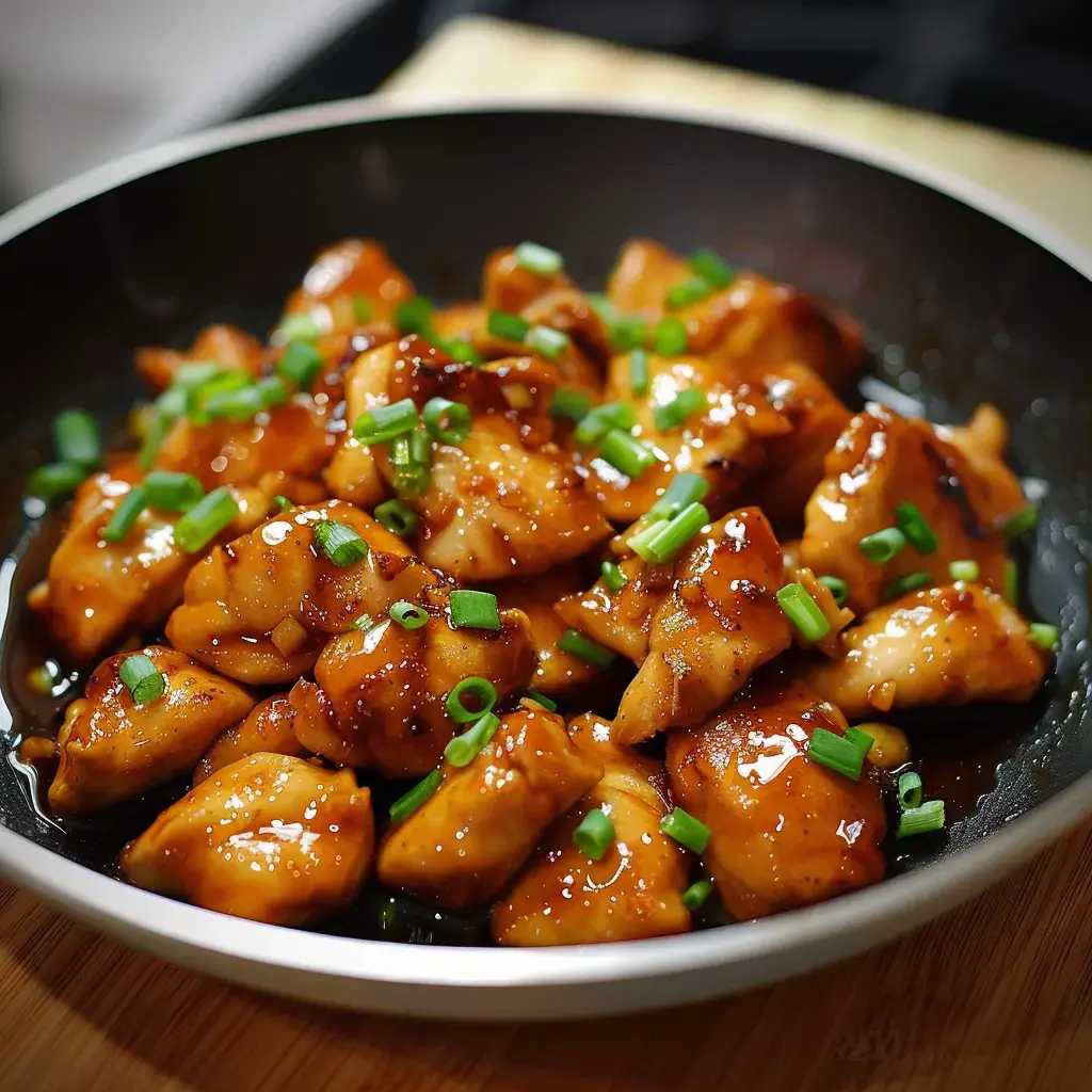 Un plat de poulet sauté en sauce sucrée, garni de ciboulette hachée, servi dans un bol noir.