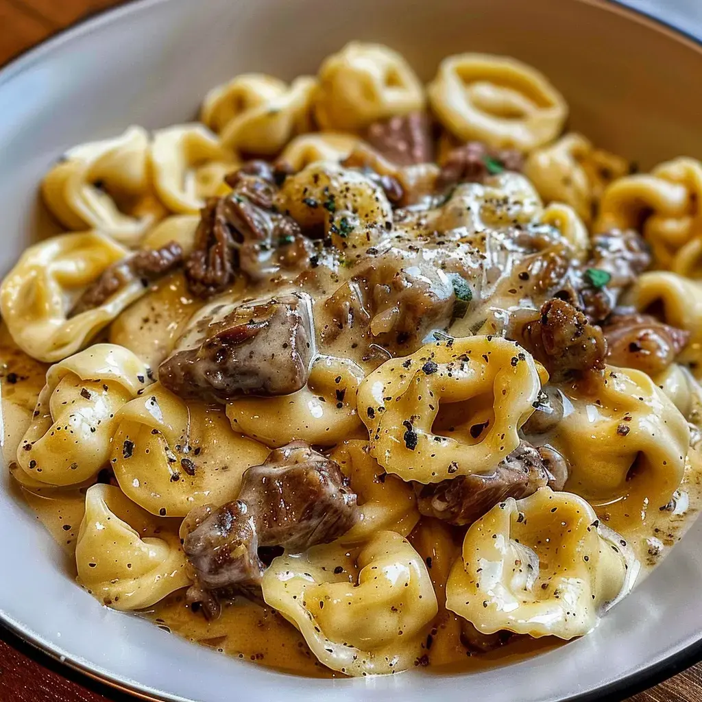 Un plat de pâtes tortellinis crémeuses avec des morceaux de viande et des épices, servi dans un bol.