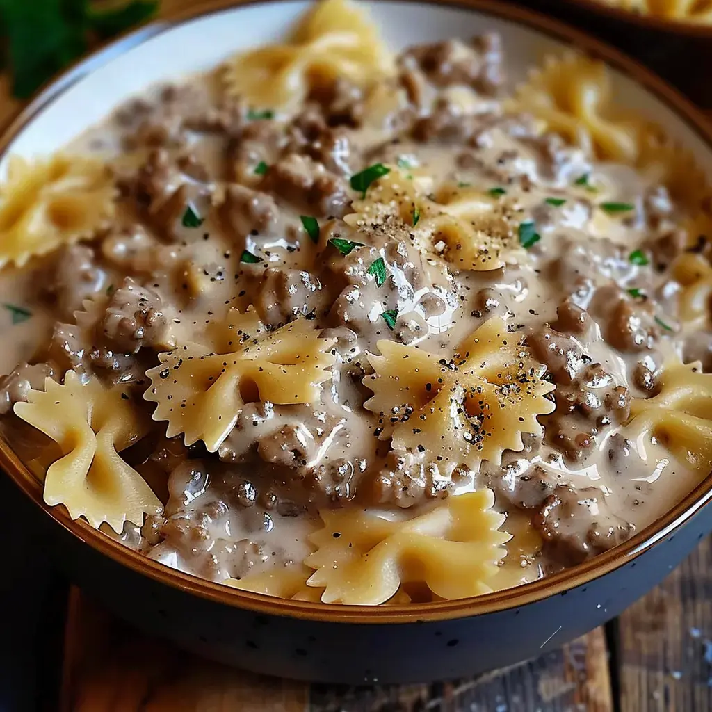 Un bol de pâtes en forme de papillon nappées d'une sauce crémeuse à la viande hachée, garnies de poivre et de persil.