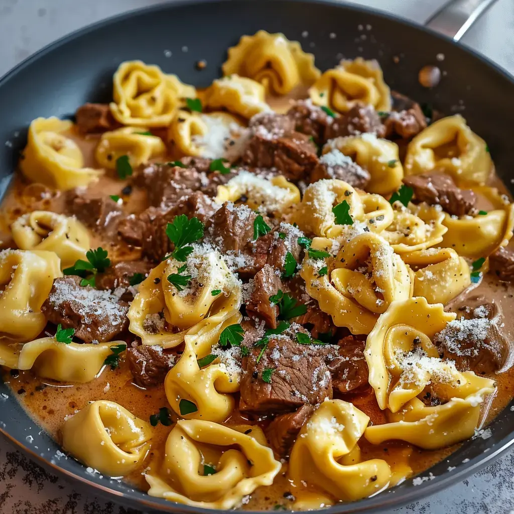 Un plat de pâtes tortellini crémeux servi avec des morceaux de viande de bœuf et garni de parmesan et de persil.