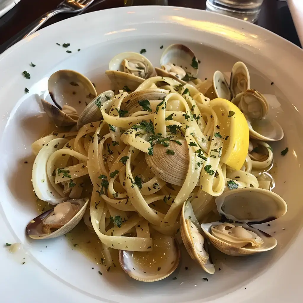 Un plat de pâtes aux palourdes, agrémenté de citron et de persil, servi dans une assiette blanche.