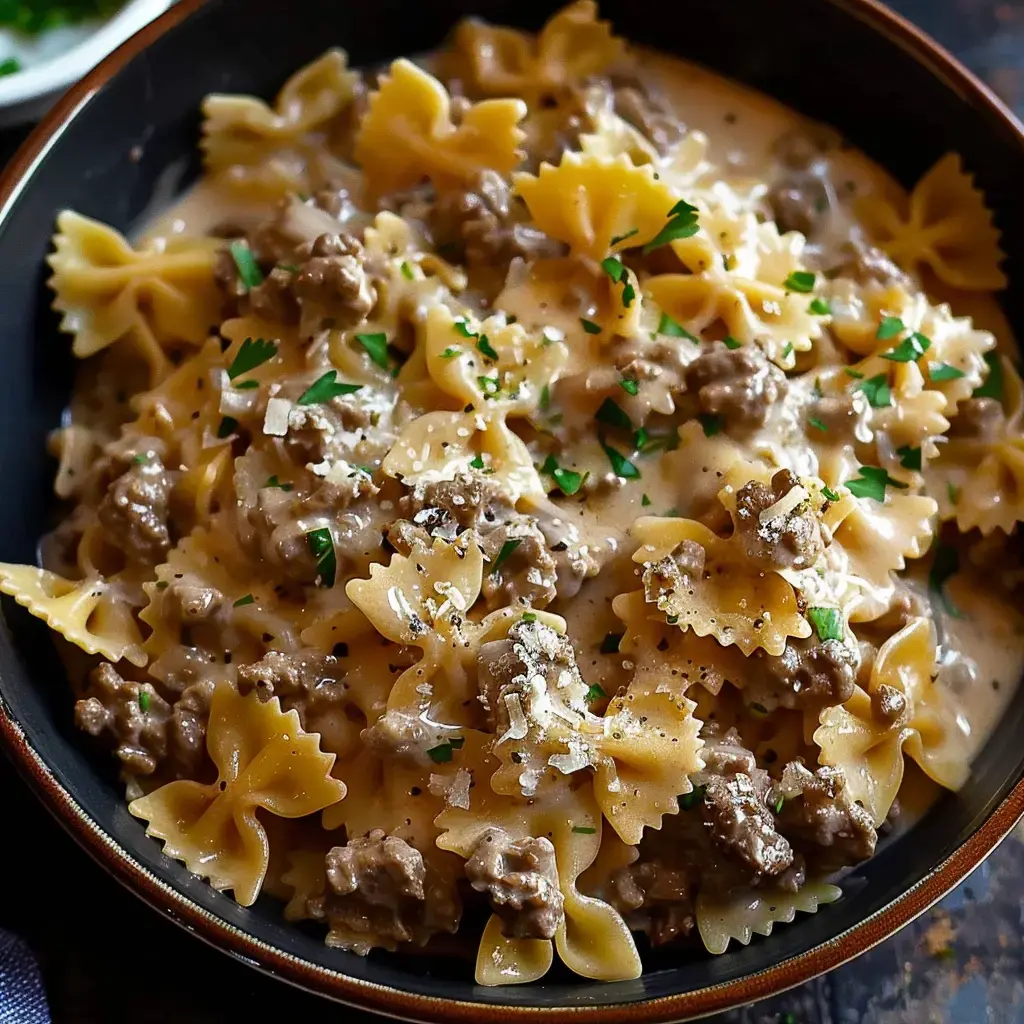 Un plat de pâtes en forme de papillon avec de la viande hachée et une sauce crémeuse, garni de persil.