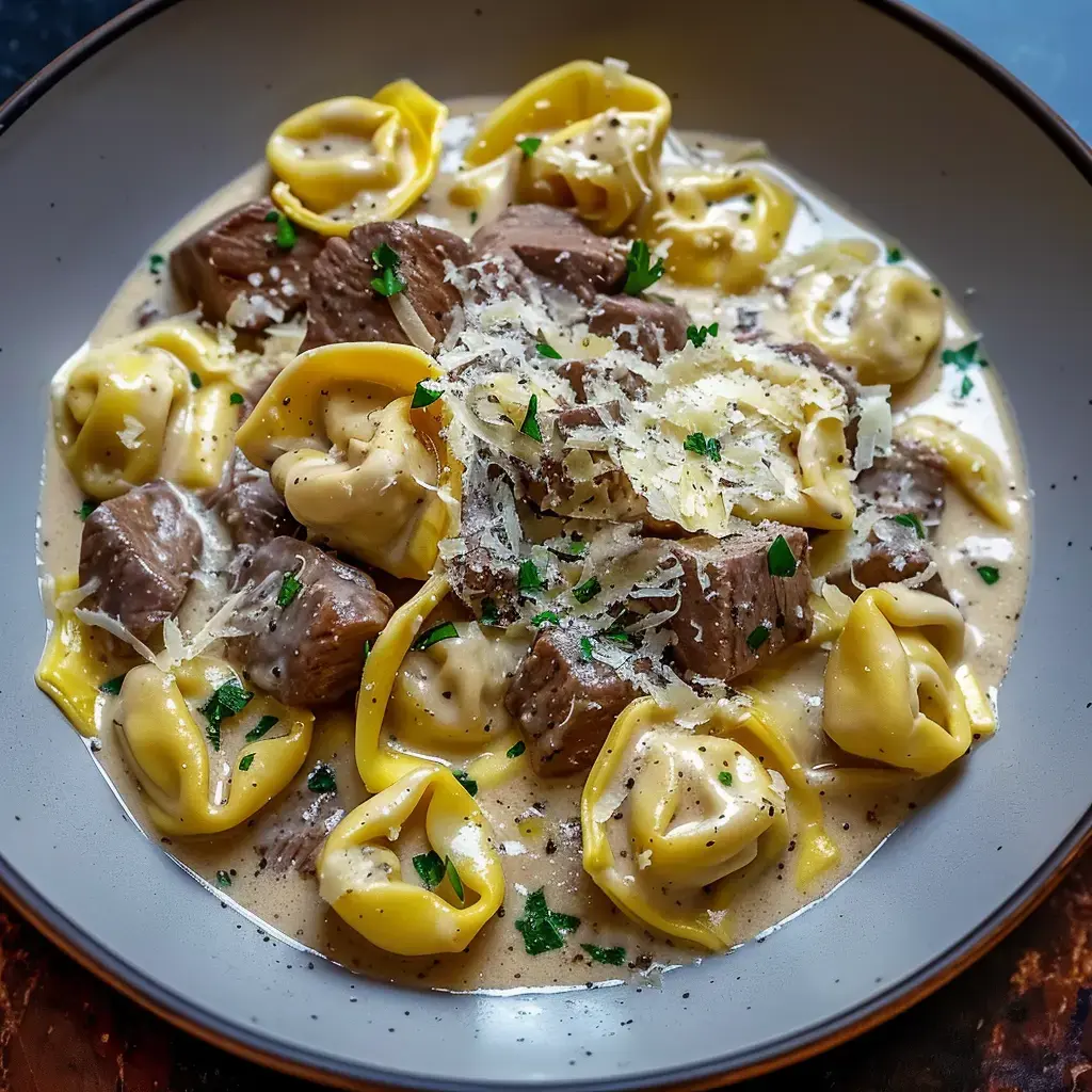 Un plat de pâtes tortellini accompagnées de morceaux de viande, le tout dans une sauce crémeuse, garni de fromage râpé et de persil.