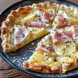 Une tarte salée découpée en parts avec du jambon, des pommes de terre, et des assaisonnements, servie sur une assiette.