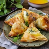 Des samoussas dorés et garnis de fromage crémeux sont présentés sur une assiette, accompagnés de jeunes pousses.