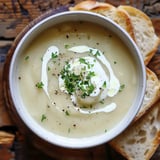 Une soupe crémeuse garnie de crème fraîche et de persil, accompagnée de tranches de pain.