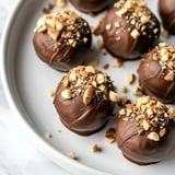 Des boules en chocolat décorées de morceaux de noix sur une assiette blanche.