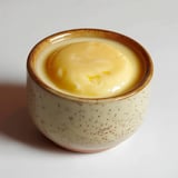 Un petit bol en céramique contenant une crème ou un dessert de couleur jaune.