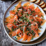 Plat de saumon fumé finement tranché, garni de câpres et de ciboulette, servi avec des tranches de pain.