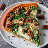 Une part de tarte à la courge garnie d'épinards, de fromage et de noix de pécan sur une assiette.