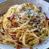 Une pile de spaghettis au bacon, au piment et au pecorino, servie sur un plateau.