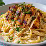 Une portion de Spaghetti Crémeux au Poulet Grillé, avec des herbes et des légumes, est servie dans un bol.