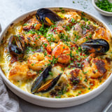Une cassolette de fruits de mer à la créole, remplie de moules, de langoustines et de tomates, est servie sur une table.