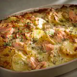 Une gratinée de pommes de terre au saumon et aneth, servie dans un plat en céramique.