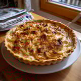 Une tarte à l'oignon et au reblochon est servie sur un plateau.