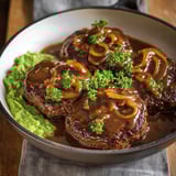 Une hamburger steak avec une sauce et des broccolis.