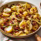 Une poêlée paysanne aux endives, avec des légumes et du bacon, est servie sur une table.