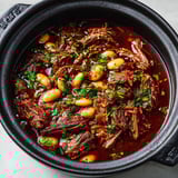 Une casserole de bœuf braisé au vin rouge et aux épices, accompagnée de haricots blancs.