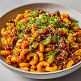 Un plat de macaronis au bœuf et au gochujang, avec des herbes vertes et des grains de riz.