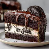 Un gâteau façon Oreo XXL est présenté sur un plateau, avec une portion de crème chantilly et des noix de cacao.