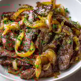 Une assiette de bœuf fondant aux oignons caramélisés, servie dans un bol blanc.