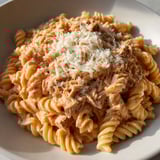 Une plate de pâtes au thon, avec une sauce tomate et des herbes, est servie sur une table.