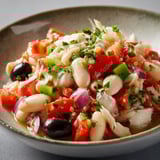 Une salade de tomates et d'olives, avec des herbes et des légumes, est servie dans un bol.
