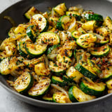 Une assiette de courgettes grillées avec des herbes et des légumes verts.