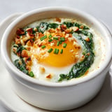 Une cocotte d'œufs à la florentine et sauce pilpil est servie sur un plateau.