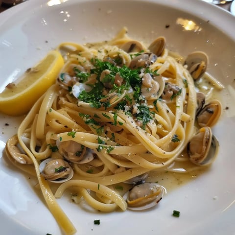 Un plat de linguine aux palourdes garni de persil et accompagné d'une tranche de citron.