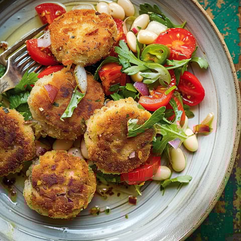Une salade de haricots blancs, croquettes de sardines et tomates confites est servie sur un plateau.