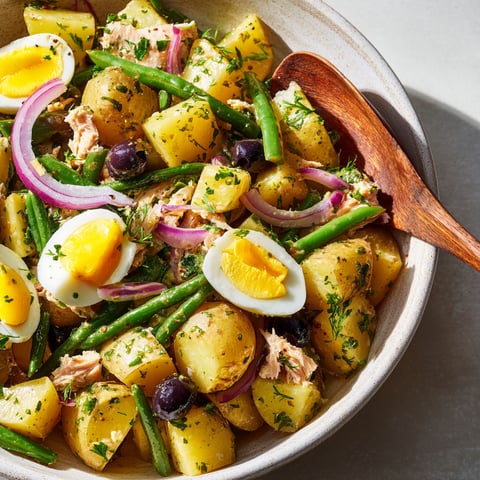 Une salade de pommes de terre, haricots verts, thon et œufs est servie dans un bol.