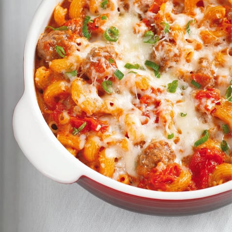 Une casserole de macaronis aux tomates et aux saucisses italiennes est servie dans un bol en verre.