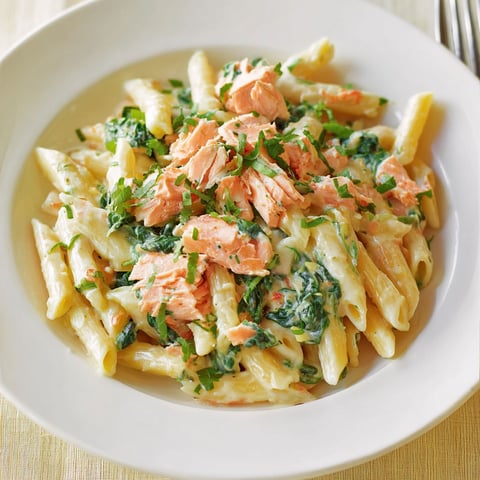 Une assiette de pâtes à la crème et au saumon, garnie de pâte de cilantro et de légumes verts.