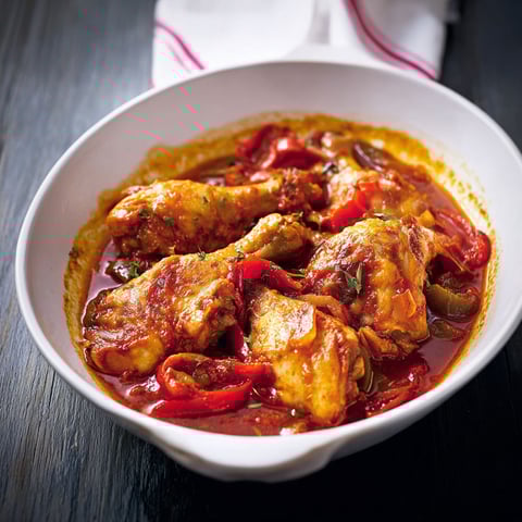 Un plat de poulet basquaise, avec des tomates, des oignons et des épinards, est servie sur une table.