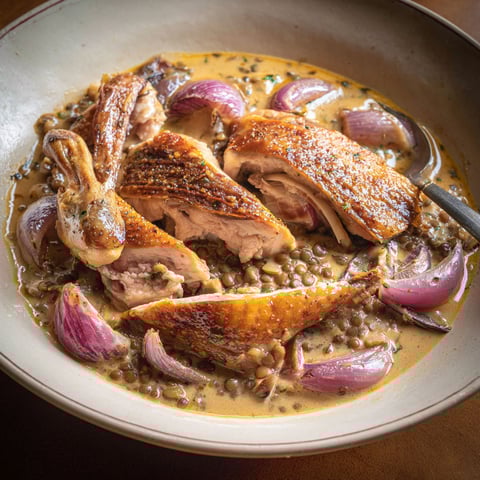 Une assiette de pintade à l'auvergnate, avec des légumes et des herbes, est servie sur une table.