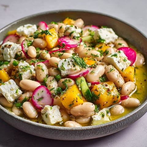 Une salade de haricots borlotti, feta et mangue est servie dans un bol en acier.